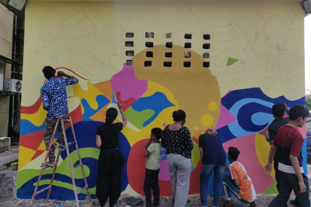 A group of boys and girls painting a wall mural with their backs to the camera
