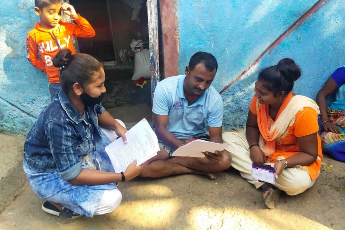 Two women and a man sitting in front of a house and going over documents, while a child looks on