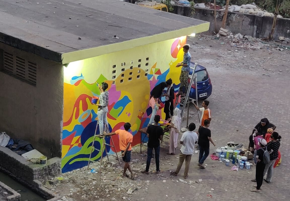 A wall being painted in bright colours by a group of young girls and boys