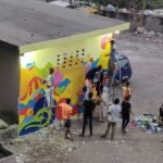 A wall being painted in bright colours by a group of young girls and boys